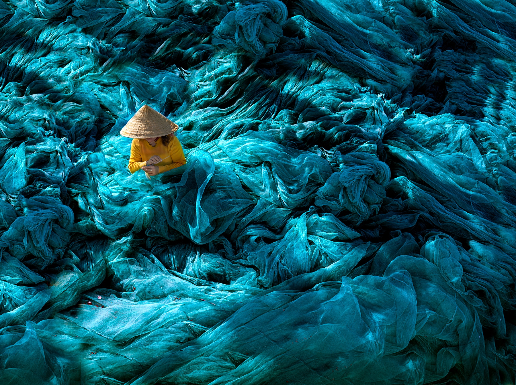 Immerse yourself in a sea of nets: a Vietnamese woman surrounded by vibrant blue netting, blending tradition with artistry and wonder.